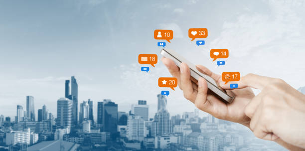 istock Hand holding mobile smart phone, with notification icons and city background 1046302482