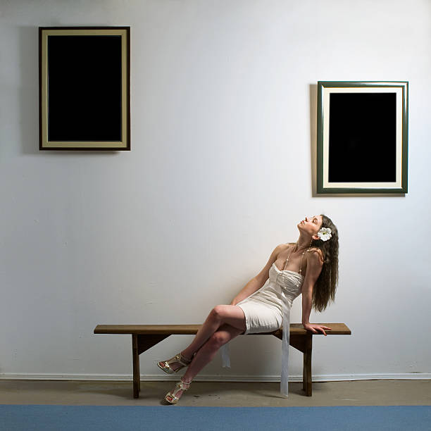 Cute teen girl in glasses sitting in the artist's studio. Girl holding a blank picture frame. Contemporary art . Empty picture frames hanging on the wall. Space for text.