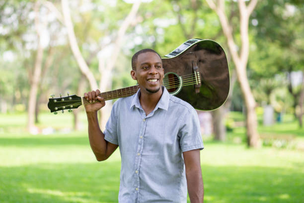 istock Happy black man holding guitar on shoulder in park 1046346466
