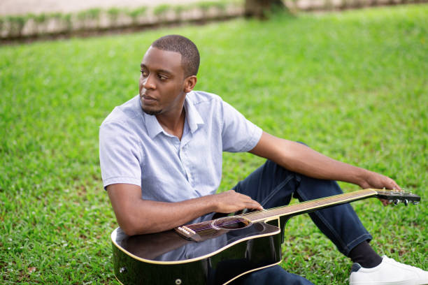 istock Pensive black man holding guitar and sitting on grass 1046346520