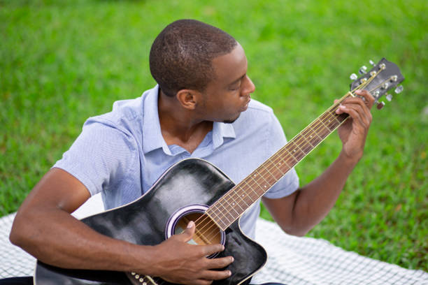 istock Serious black man playing guitar and sitting on ground in park 1046346550