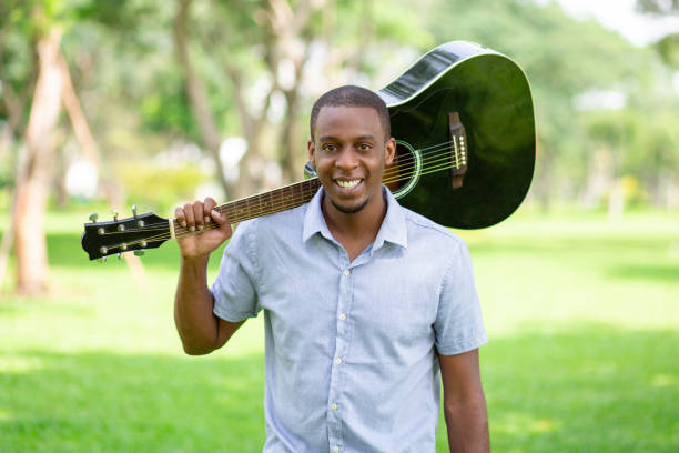 istock Smiling black man holding guitar on shoulder in park 1046346566