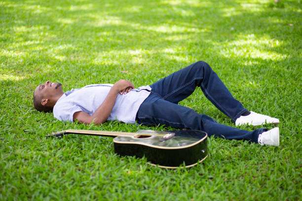 homme noir couché sur l’herbe avec guitare en parc souriant - musical instrument nature outdoors musician photos et images de collection