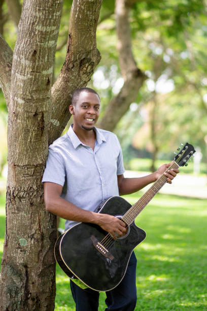 istock Smiling black man playing guitar and leaning on tree 1046346596