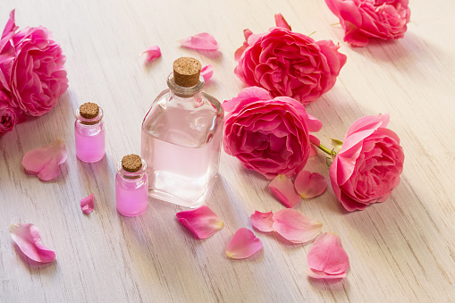 Rose oil in glass bottles and rose flower petals on white wooden background, SPA or aromatherapy concept