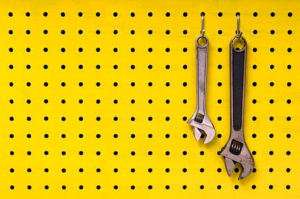 deux wrenches suspendus crochets sur jaune panneau vertical perforé - pegboard photos et images de collection