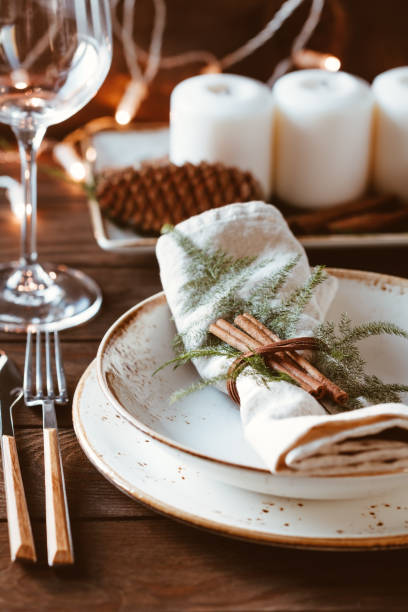 istock Thanksgiving table setting among white candles and cones. Ceramic plate with fork and knife on a linen napkin. Close up. 1046390220