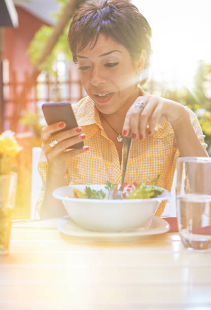 istock Beautiful young woman using smartphone while eating a salad 1046394550