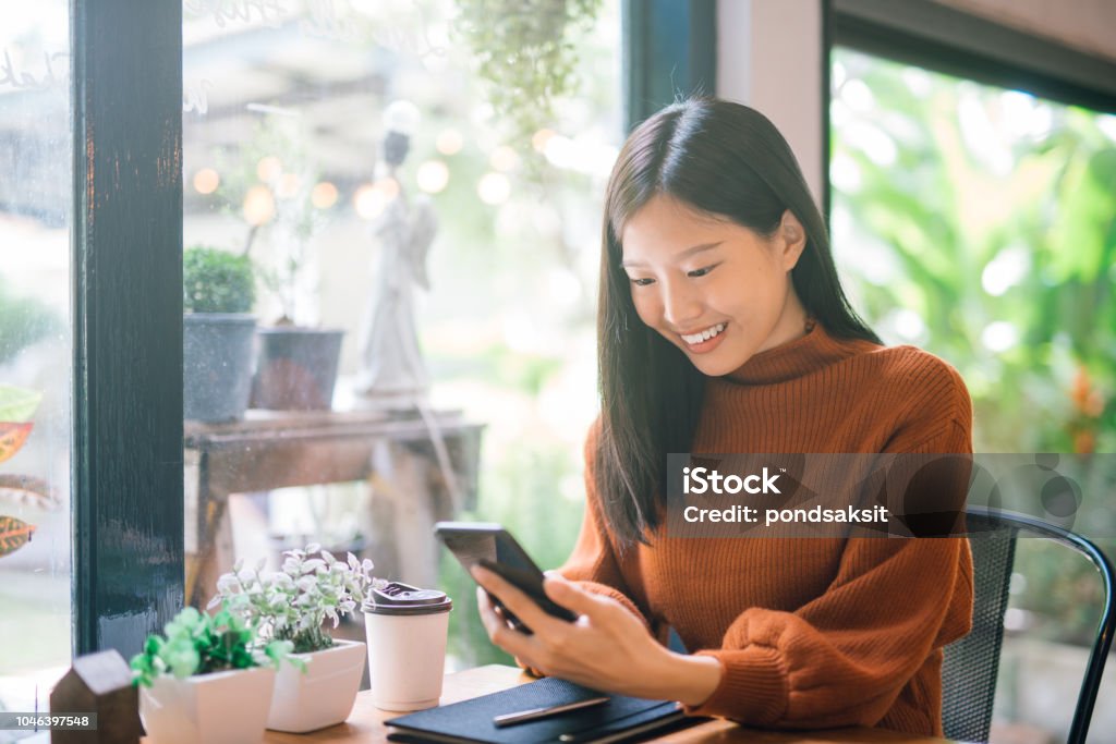 Young Asian woman using phone Young Asian woman using phone at a coffee shop happy and smile. Asian and Indian Ethnicities Stock Photo