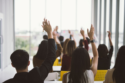 Raised up hands and arms of large group in seminar class room at Conference