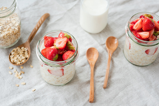 Overnight oats with strawberries and almond milk in a jar. Healthy vegan vegetarian breakfast. Bamboo wooden spoons for eating