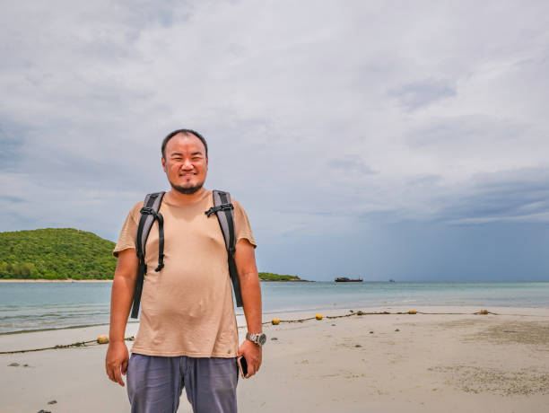 istock Asian fat Backpacker stand on the idyllic beach with Rainy cloud Sky in vacation time 1046406878