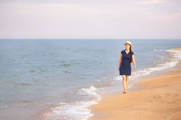 young smiling woman in dress and hat walking on the sea beach. Summer vacation concept
