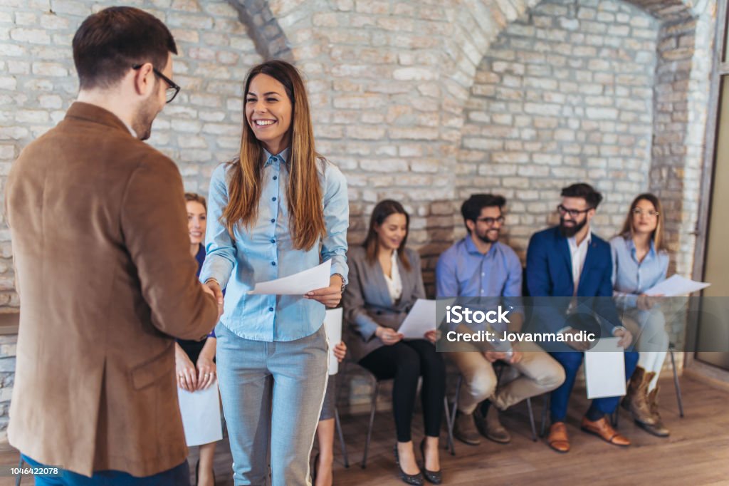 Hombre de negocios dando la mano con la mujer además de gente esperando para la entrevista de trabajo en una oficina moderna - Foto de stock de Entrevista de trabajo libre de derechos