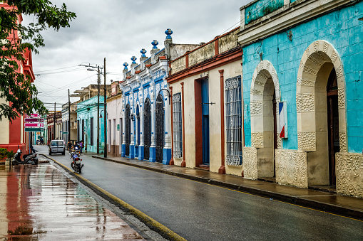 Old Spanish colonial colorful decorated living houses across the street wet after rain in the center of Camaguey, Cuba