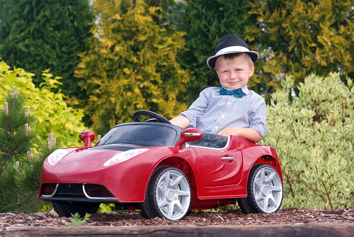 Three-year boy in a hat sits in a red toy car