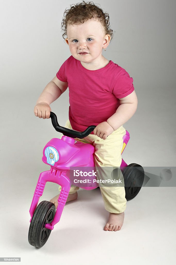Heureux bébé fille avec son rose vélo sur fond gris - Photo de Petite moto libre de droits