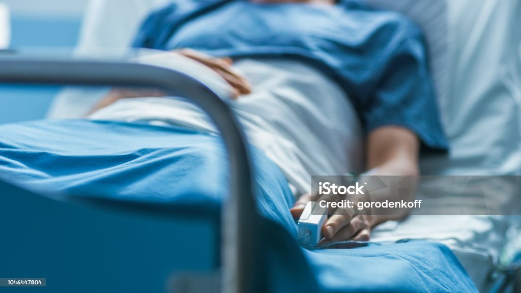 In ospedale il paziente maschio malato dorme sul letto. L'apparecchiatura di monitoraggio della frequenza cardiaca è sul dito. - Foto stock royalty-free di Ospedale