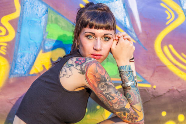 femme rebelle tatoué qui pose contre un mur - tatouage de charme photos et images de collection