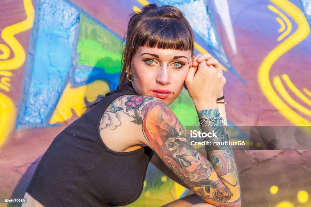 tattooed rebel girl posing against a wall tattooed rebel girl posing against a wall painted with colorful graffiti Tattoo Stock Photo