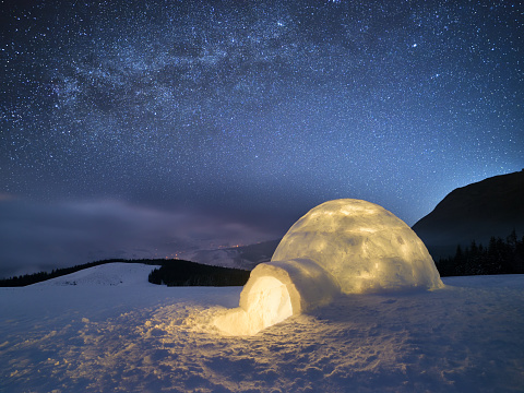 Night landscape with a snow igloo with light. Extreme house. Winter in the mountains. Sky with the stars and the Milky Way