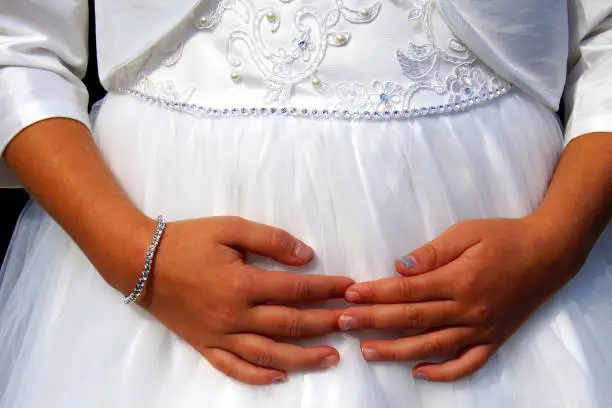 Cute little cild bridesmaid in white dress with hands on her belly