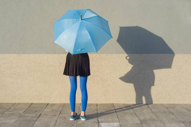Young girl under umbrella stands with gray wall background, copy space.