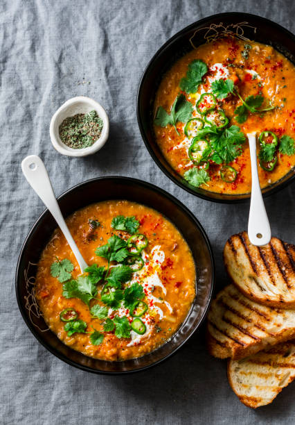 Curried red lentil tomato and coconut soup - delicious vegetarian food on grey background, top view. Flat lay served healthy lunch Curried red lentil tomato and coconut soup - delicious vegetarian food on grey background, top view. Flat lay served healthy lunch lentil photos stock pictures, royalty-free photos & images