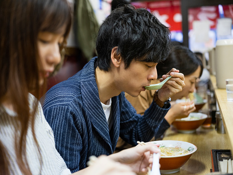 A young Chinese couple enjoys a vacation in Tokyo, Japan by having a traditional lunch in a small ramen shop.
