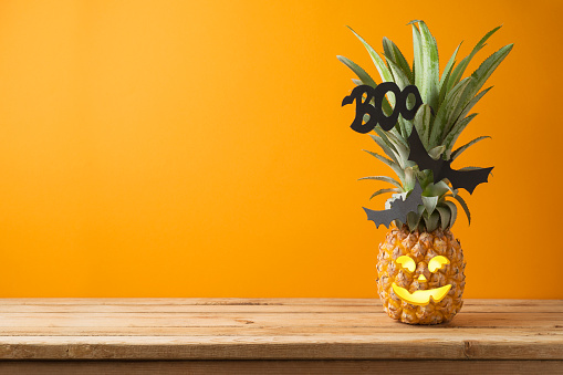 Halloween holiday concept with jack o lantern pineapple on wooden table with copy space