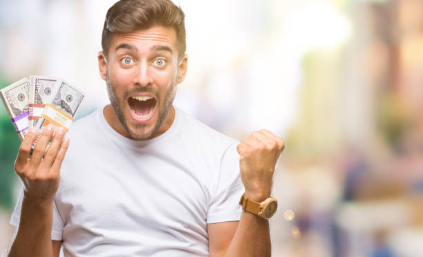 istock Young handsome man holding stack of dollars over isolated background screaming proud and celebrating victory and success very excited, cheering emotion 1046566070