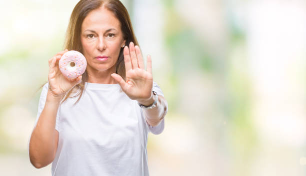 istock Middle age hispanic woman eating pink donut over isolated background with open hand doing stop sign with serious and confident expression, defense gesture 1046591246