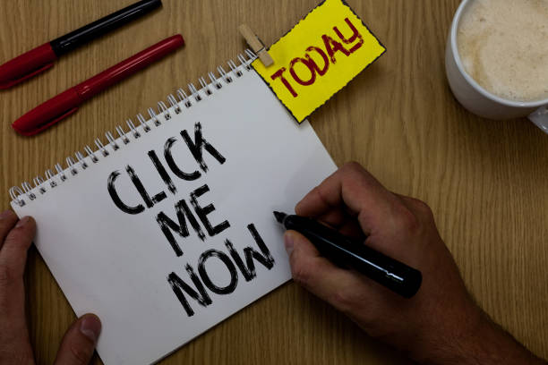 istock Handwriting text writing Click Me Now. Concept meaning Internet helping desk Press the button Online Icon Nertwork Man holding marker notebook clothespin reminder wooden table cup coffee. 1046617578