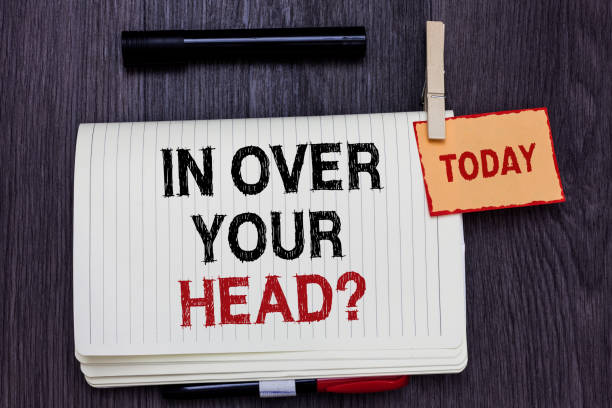 istock Handwriting text writing In Over Your Head question. Concept meaning To be involved in a difficult situation problem Written paper on wooden desk paper clip grip note with red words black pen. 1046618602