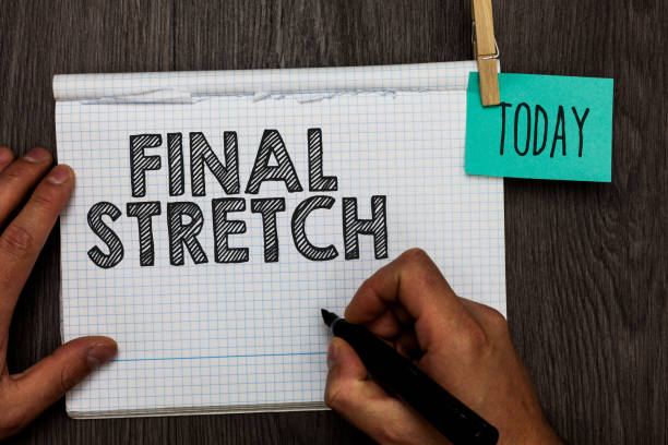 istock Handwriting text writing Final Stretch. Concept meaning Last Leg Concluding Round Ultimate Stage Finale Year ender Open notebook clothespin holding reminder clothespins clips wooden table. 1046618666