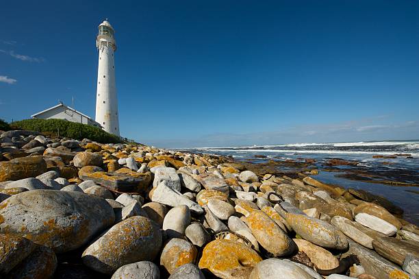 beach landscape with lighthouse and blue summer sky, south africa Beach landscape with Slangkop lighthouse, rocky shoreline and blue summer sky, Kommetjie near Cape Town, South Africa. kommetjie stock pictures, royalty-free photos & images