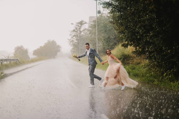 愚かな若者には、雨の日のカップル横断道路だけと結婚しました。濡れた儀式服で実行されています。 - wet dress rain clothing ストックフォトと画像