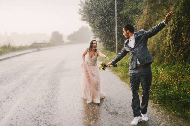 完全ウェットちょうど結婚されていたカップル ドライブ道路で雨の上を歩いてします。花嫁は彼女の夫をキャッチする訓練します。 - wet dress rain clothing ストックフォトと画像