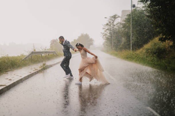 愚かな若者には、雨の日のカップル横断道路だけと結婚しました。濡れた儀式服で実行されています。 - wet dress rain clothing ストックフォトと画像