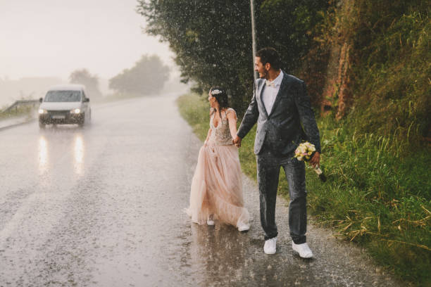 드라이브도로 지나가는 비에 완전히 젖어 그냥 결혼된 커플. 지나가는 자동차를 보고. - wet dress rain clothing 뉴스 사진 이미지