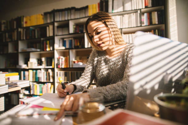 istock Cute young school girl sitting in library and taking notes. Sitting alone and studying in bright library. 1046635038