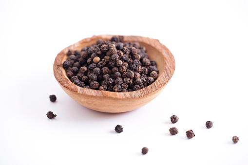 Peppercorns in wooden bowl isolated on white.