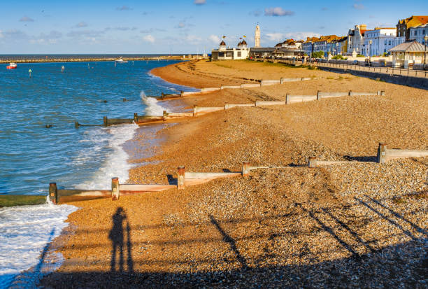 späten nachmittag herbstsonne dreht die kieselsteine am strand und hölzernen buhne wasser brecher in herne bay, kent, uk eine goldgelbe farbe. ein schatten von einem photogpraher kann gesehen werden, an einen zaun gelehnt - herne stock-fotos und bilder