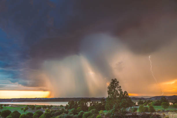 A massive rain cloud approaches as a storm rain breaks over Ayamonte, Andalusia Spain and the Guadiana river at sunset. The sky is golden behind the clouds and there is a lightning strike.