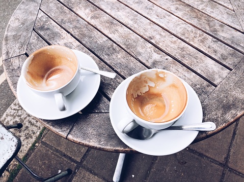 Pair of empty coffee cups sitting on the edge of a rustic wooden table at a street cafe