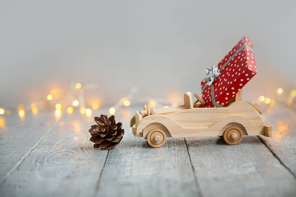 wooden car with gift on a wooden gray background and lights from the garland. Christmas concept wooden car with a beautiful red gift with a bow on a wooden gray background and lights from the garland. Christmas card wooden car stock pictures, royalty-free photos & images