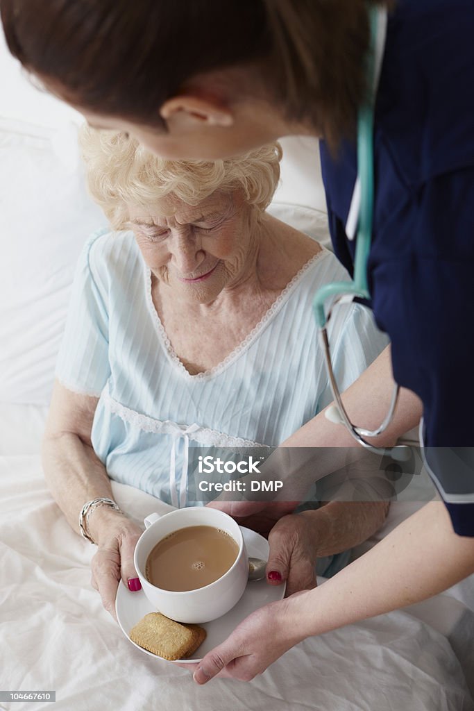 Infirmière donnant Femme âgée une tasse de thé dans la chambre - Photo de Biscuit libre de droits