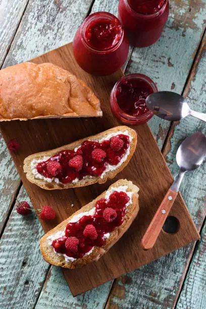 Homemade berry jam with fresh raspberries and currants on ciabatta toasts on wooden cutting boards overhead view