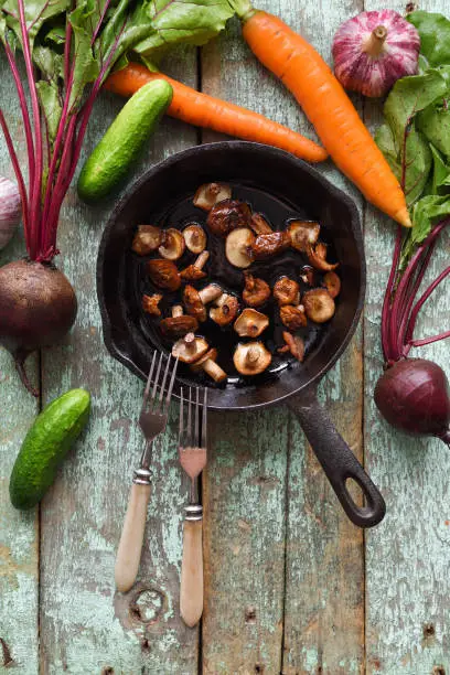 Tasty nutritious vegetarian meal. Fried Slippery Jack mushrooms (Suillus luteus) in cast iron pan with raw cucumbers, beets and carrots on shabby blue background copyspace top view