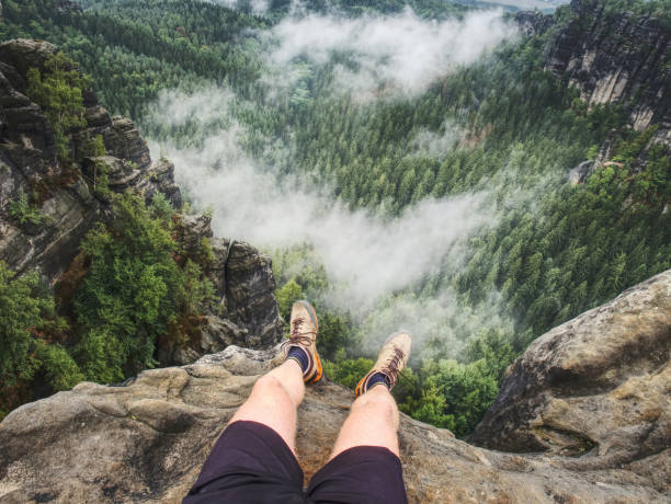 Hiker man take a rest on mountain peak. Male legs on sharp summit and hiker enjoy spectacular view.